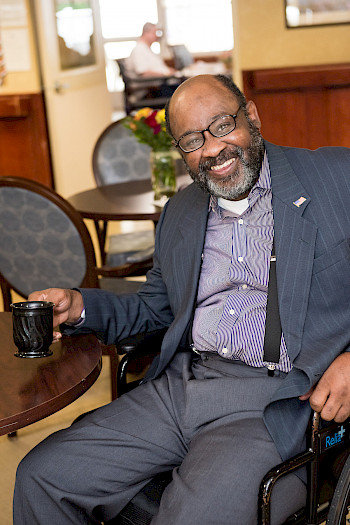 Resident in wheelchair drinking coffee in the dining room of 60 West, Rocky Hill